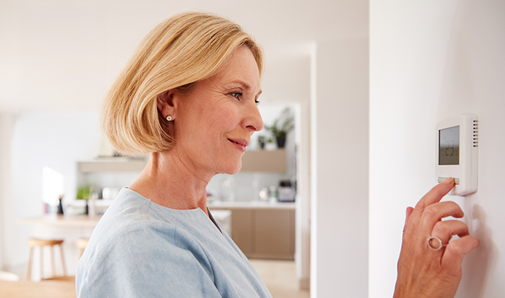 Resident adjusting thermostat to keep apartment cool and maintain energy efficiency during summer
