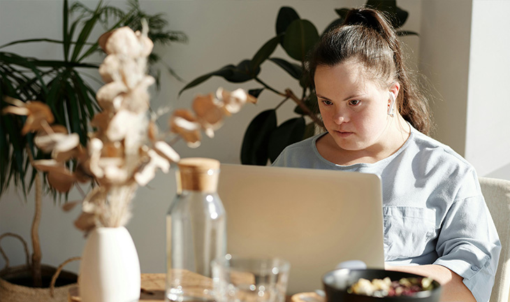 Woman working from home in a modern apartment workspace, using a laptop and taking notes