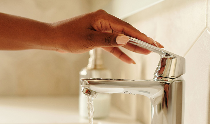 Resident using water efficiently in a modern apartment kitchen with reusable items and sustainable everyday habits.
